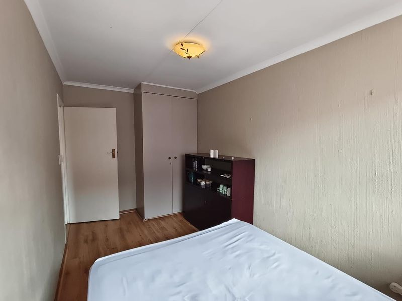 A bedroom featuring laminate flooring, a built-in wardrobe, and neutral wall finishes, providing a functional and well-lit living space.