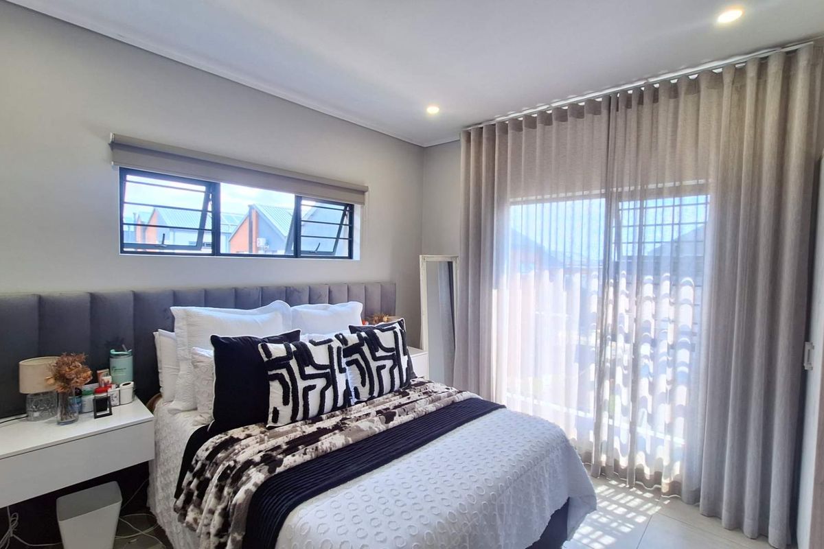 A well-maintained bedroom featuring an upholstered headboard, tiled flooring, recessed lighting, and large sliding glass doors with floor-to-ceiling curtains.
