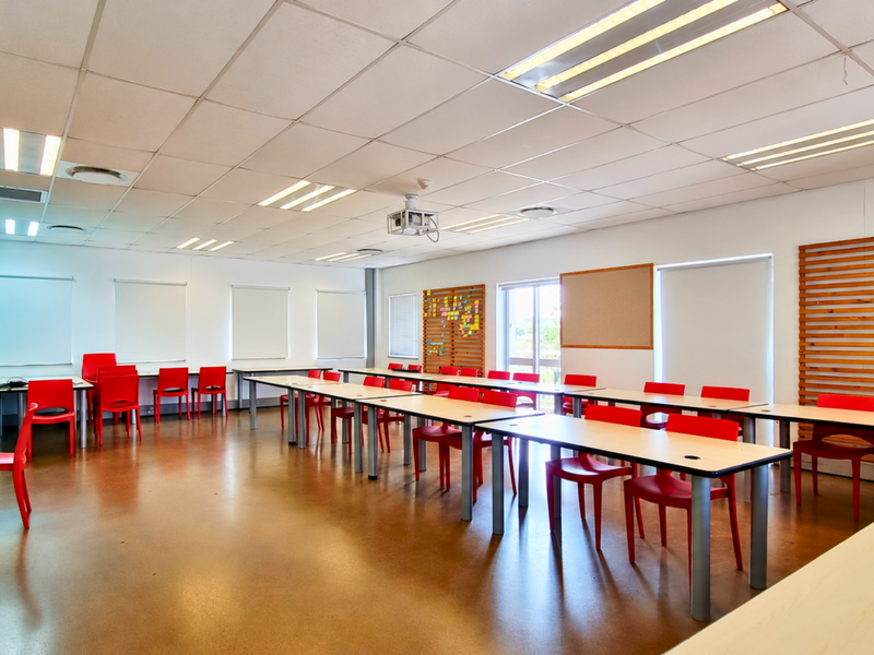 A spacious, well-lit office or training room featuring a suspended ceiling, recessed lighting, and integrated projector, suitable for collaborative work or presentations.