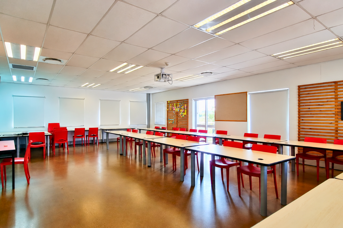A spacious, well-lit office or training room featuring a suspended ceiling, recessed lighting, and integrated projector, suitable for collaborative work or presentations.