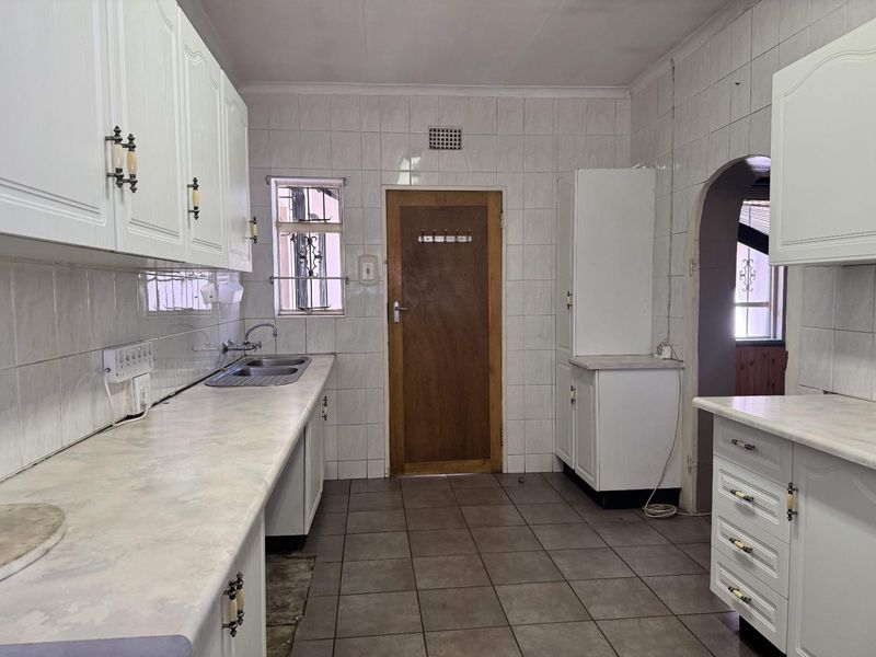 A functional kitchen featuring white built-in cabinetry, laminate countertops, a double bowl sink, and fully tiled walls and floors.
