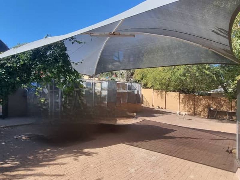 Rear outdoor area featuring a large shade sail, paved ground surface, and perimeter boundary walling.