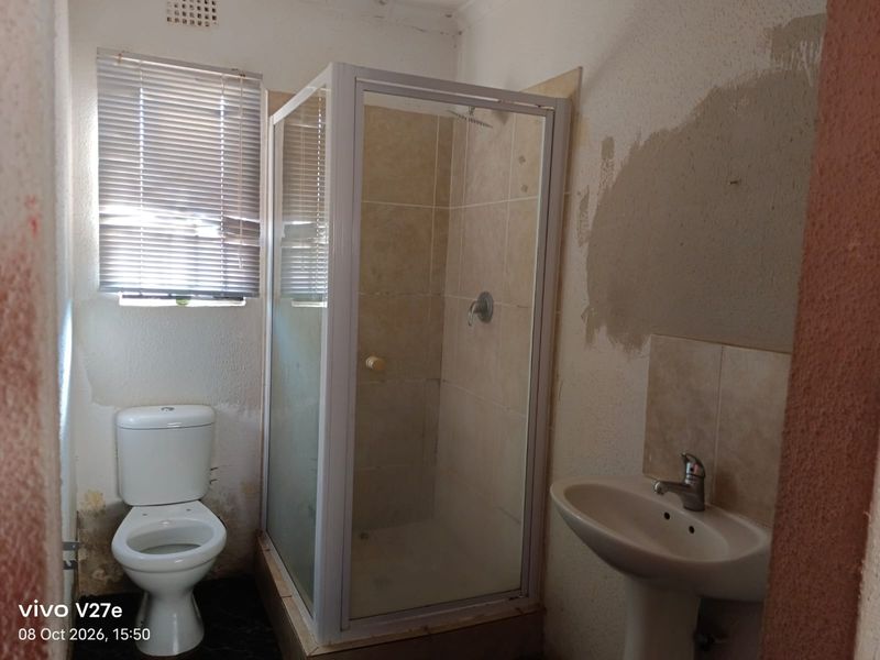 A small bathroom featuring a shower enclosure, pedestal basin, and toilet, currently requiring wall repairs and cosmetic updates to improve the overall condition.