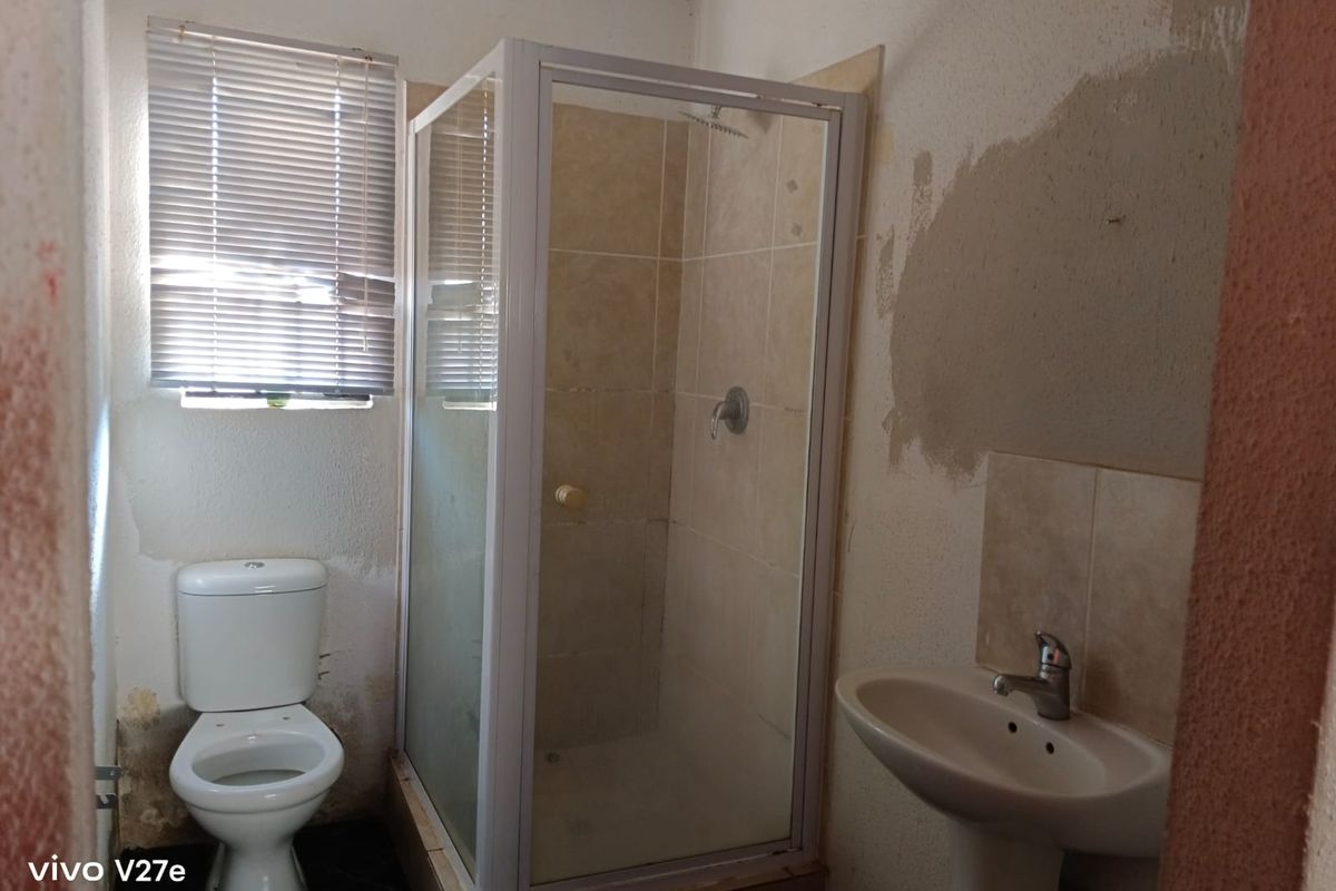A small bathroom featuring a shower enclosure, pedestal basin, and toilet, currently requiring wall repairs and cosmetic updates to improve the overall condition.