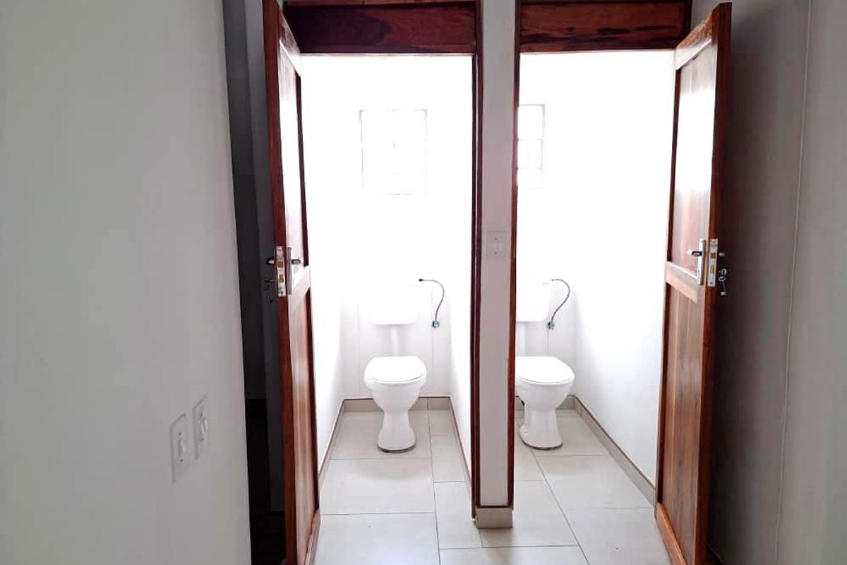 Two separate restroom cubicles featuring white ceramic toilets, tiled flooring, and wooden door frames within an office environment.