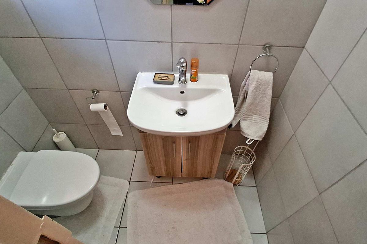 A compact bathroom featuring a wall-mounted toilet, a vanity basin with storage cabinet, and neutral floor-to-ceiling wall tiling.