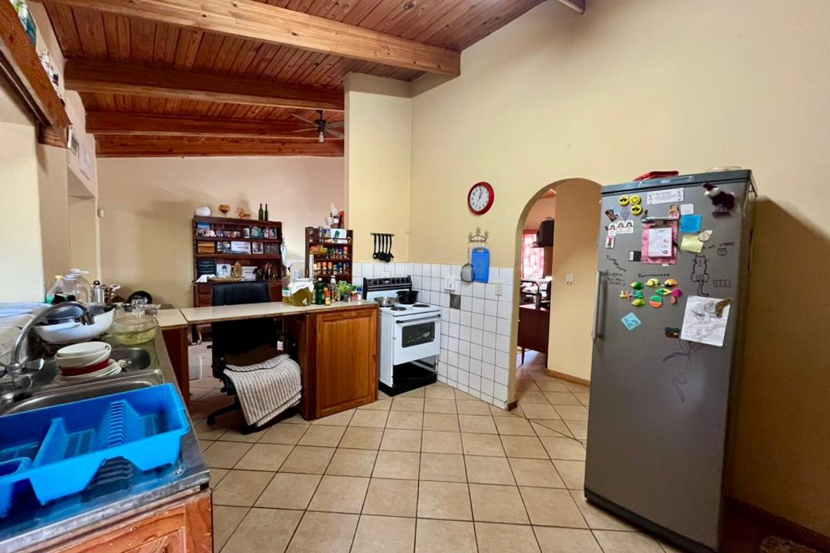 A functional kitchen featuring exposed timber beam ceilings, tiled flooring, a freestanding stove, and an arched doorway leading to adjacent living spaces.