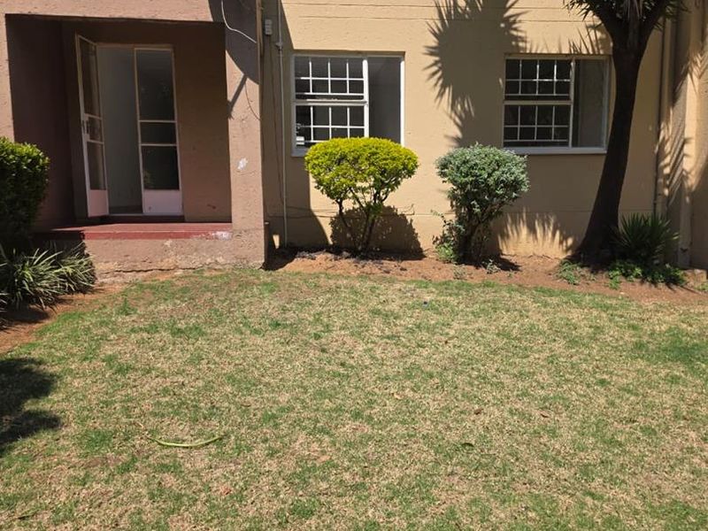 Rear view of the apartment building featuring a small private lawn area, security gates, and window bars.