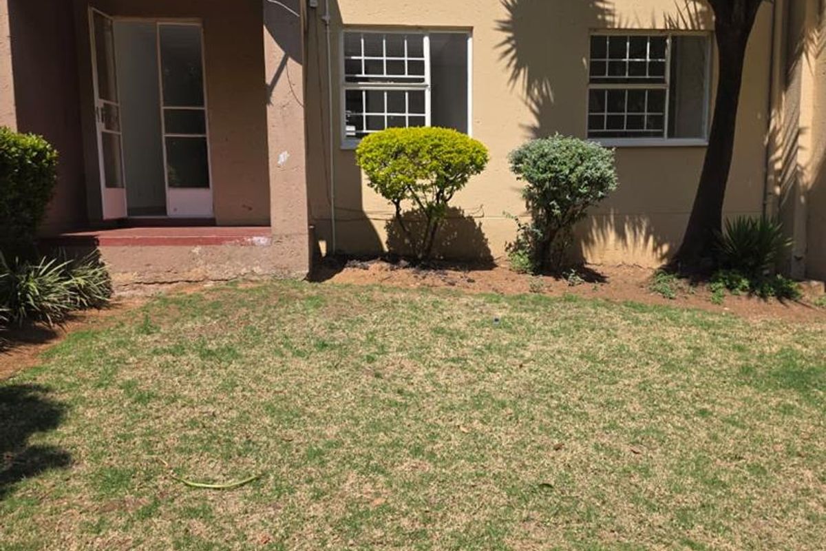 Rear view of the apartment building featuring a small private lawn area, security gates, and window bars.