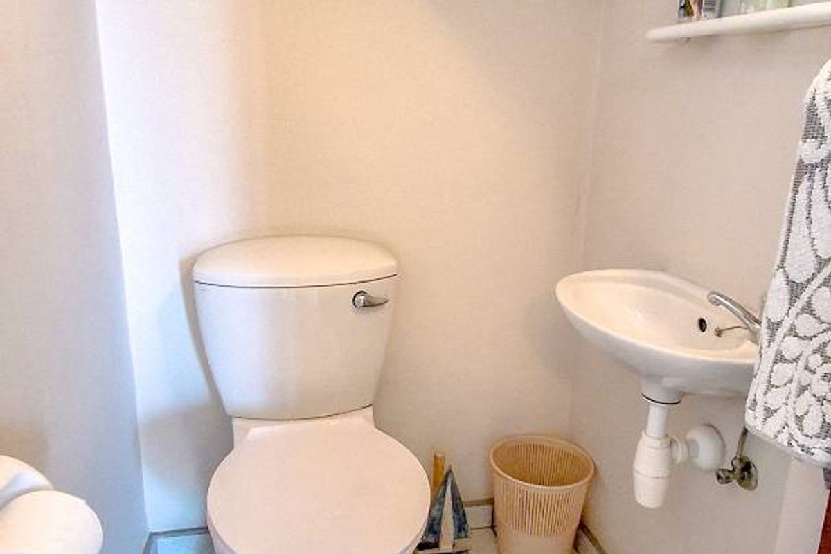 A compact guest bathroom featuring a white toilet, wall-mounted basin, and tiled flooring with built-in storage shelving.