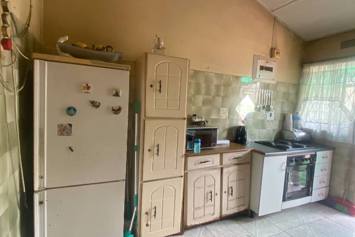 A dated kitchen featuring tiled flooring, a tiled backsplash, built-in cabinetry, and a vaulted ceiling, offering potential for modernization.