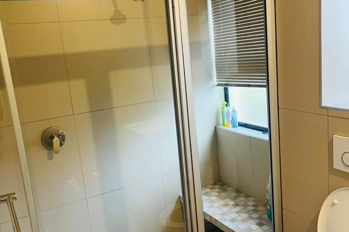 A functional bathroom featuring a shower enclosure with a built-in tiled bench, neutral wall tiling, and a standard toilet.