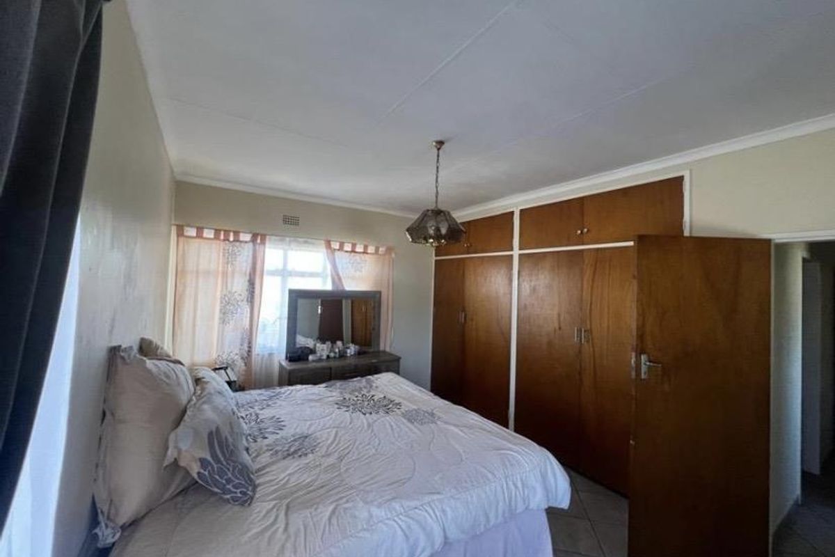 A bedroom featuring built-in wooden cupboards, tiled flooring, and a central light fixture, offering a functional space with potential for modern updates.
