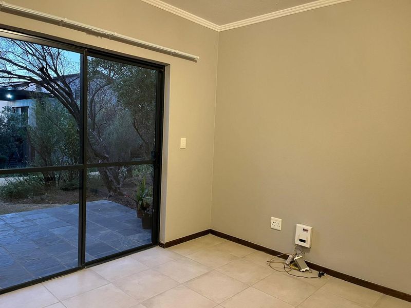 An empty living room featuring neutral walls, tiled flooring, and a large sliding glass door providing access to an outdoor patio area.