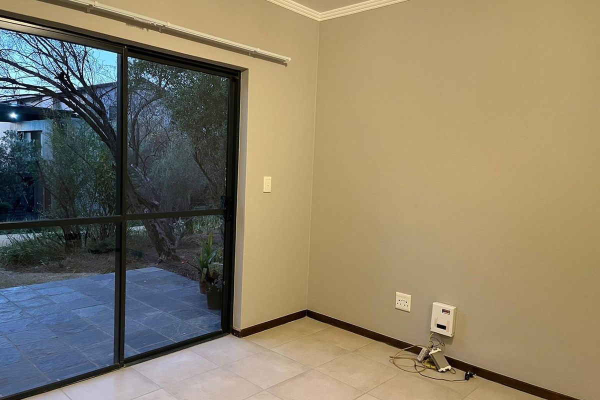 An empty living room featuring neutral walls, tiled flooring, and a large sliding glass door providing access to an outdoor patio area.