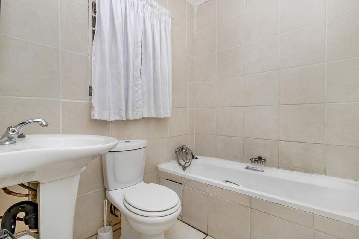 A functional bathroom featuring a pedestal sink, a standard toilet, and a tiled bathtub with wall-mounted shower fixtures.