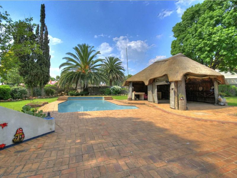 Outdoor pool area featuring a swimming pool, brick paved patio, and a traditional thatched lapa structure set within a landscaped garden.