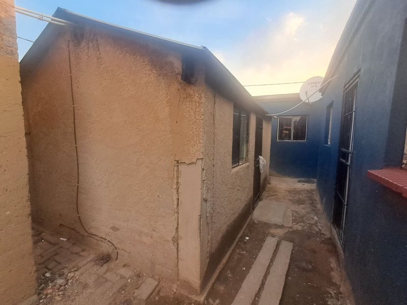A narrow exterior side passage between two structures showing significant wear to the exterior plaster and paintwork.