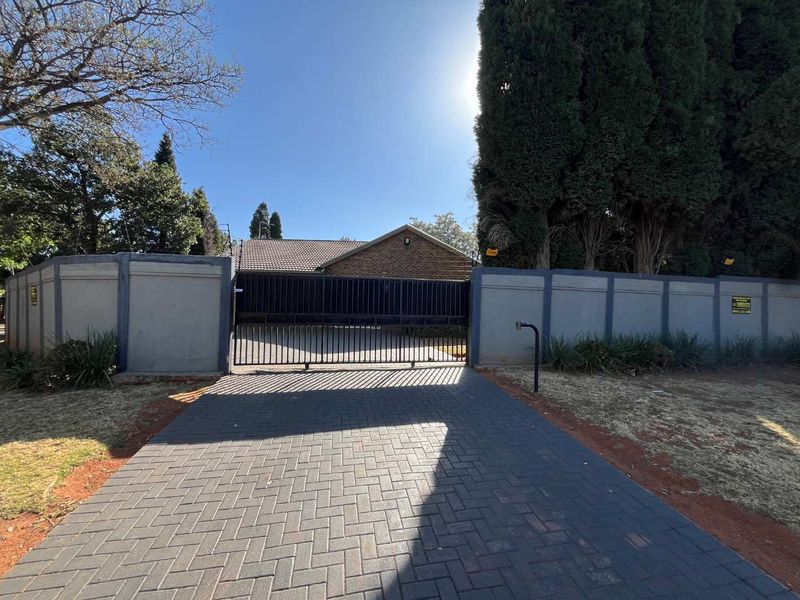 Front view of the property featuring a paved driveway, secure perimeter wall, and a sliding metal gate leading to the main residence.