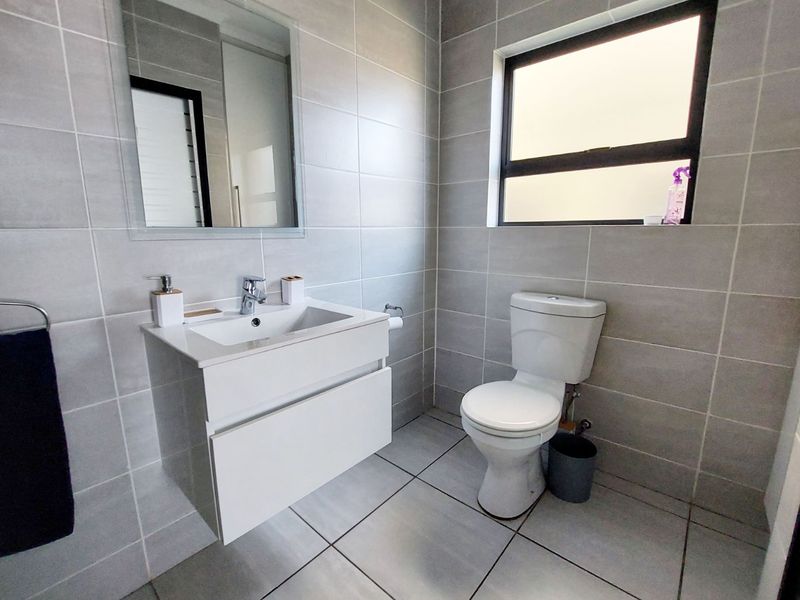 Modern bathroom featuring grey wall and floor tiles, a wall-mounted vanity with a ceramic basin, and a contemporary toilet.