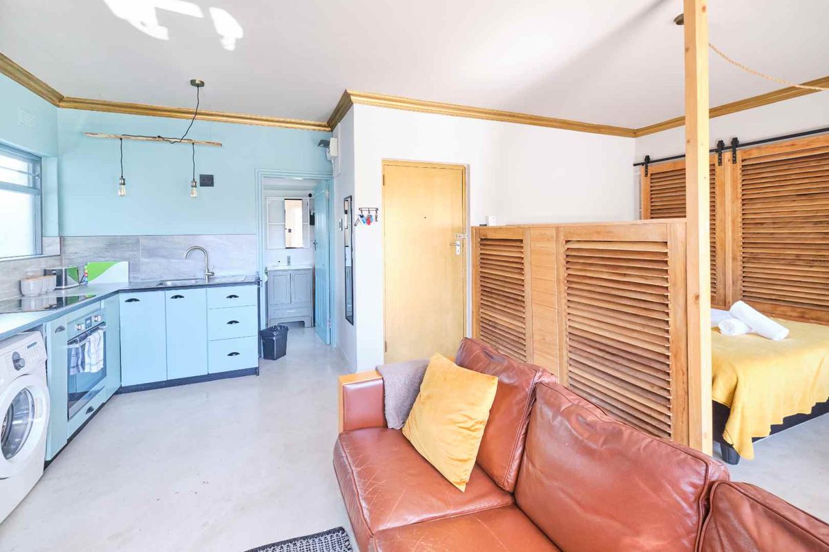 Open-plan studio apartment featuring a compact kitchen with built-in cabinetry, integrated appliances, and a louvered partition separating the living and sleeping areas.