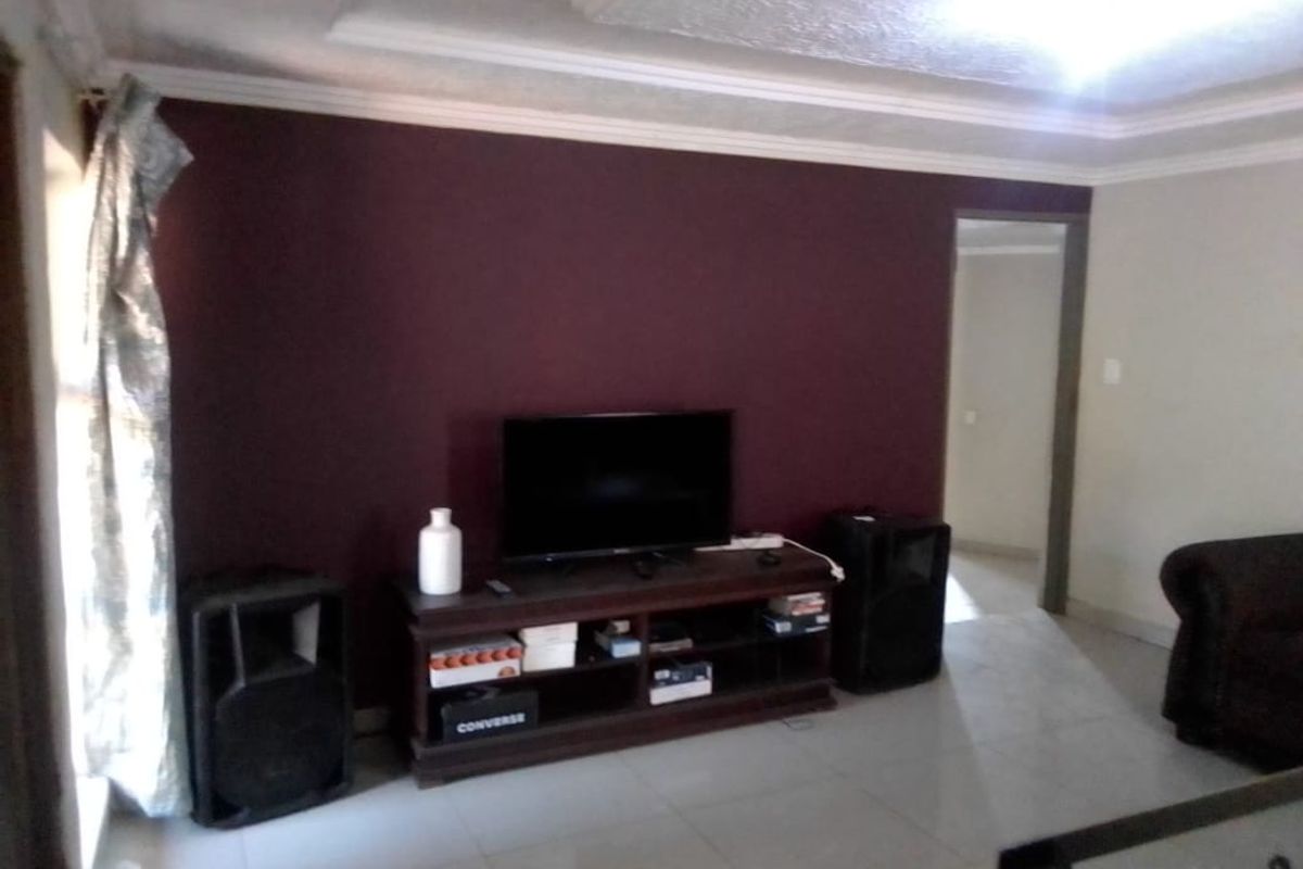 A living room featuring a dark accent wall, tiled flooring, and decorative ceiling cornices.