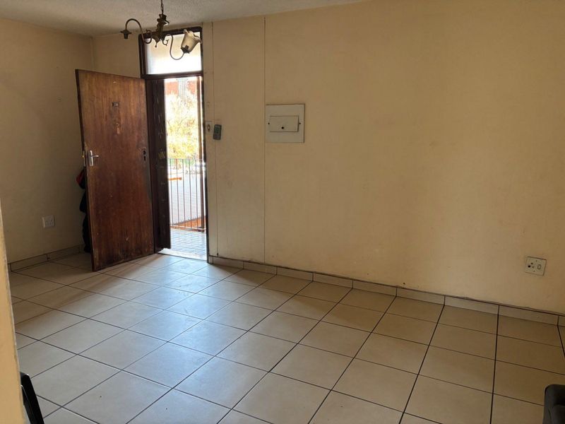 An empty entrance area featuring tiled flooring, a main door, and an electrical distribution board, presenting a blank canvas for renovation.