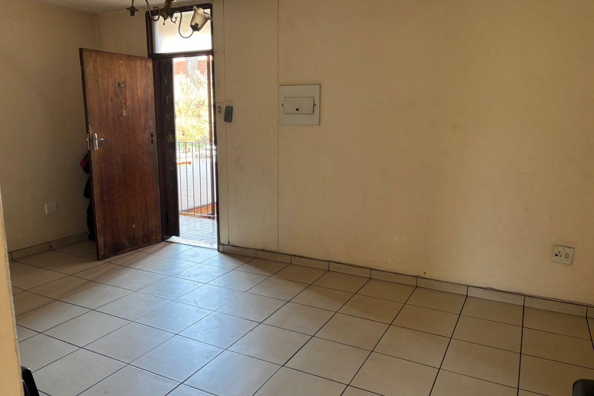 An empty entrance area featuring tiled flooring, a main door, and an electrical distribution board, presenting a blank canvas for renovation.