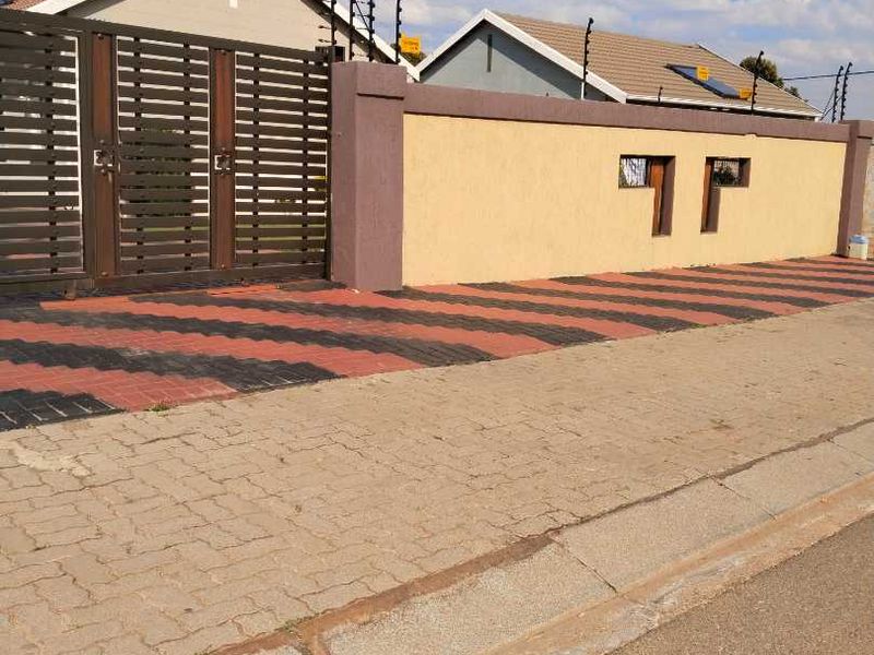 Front view of the property featuring a secure perimeter wall with electric fencing, a sliding gate, and a paved driveway.