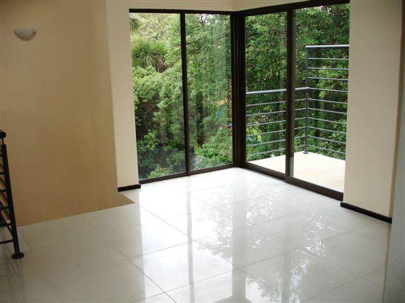 Bright living area featuring polished porcelain floor tiles and large sliding glass doors opening onto a private balcony with lush garden views.