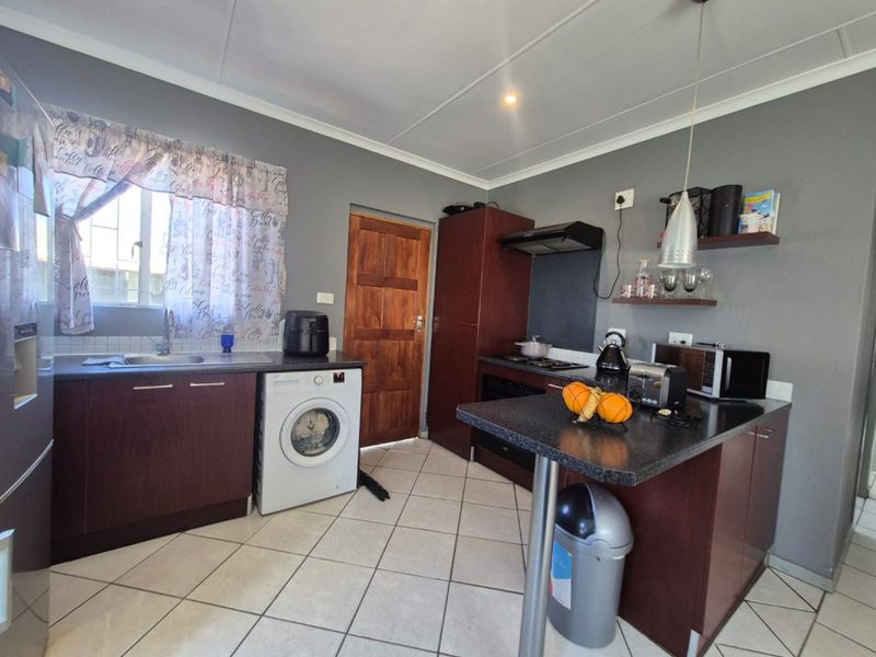 Functional kitchen featuring dark wood cabinetry, a breakfast bar, integrated hob and oven, and tiled flooring.
