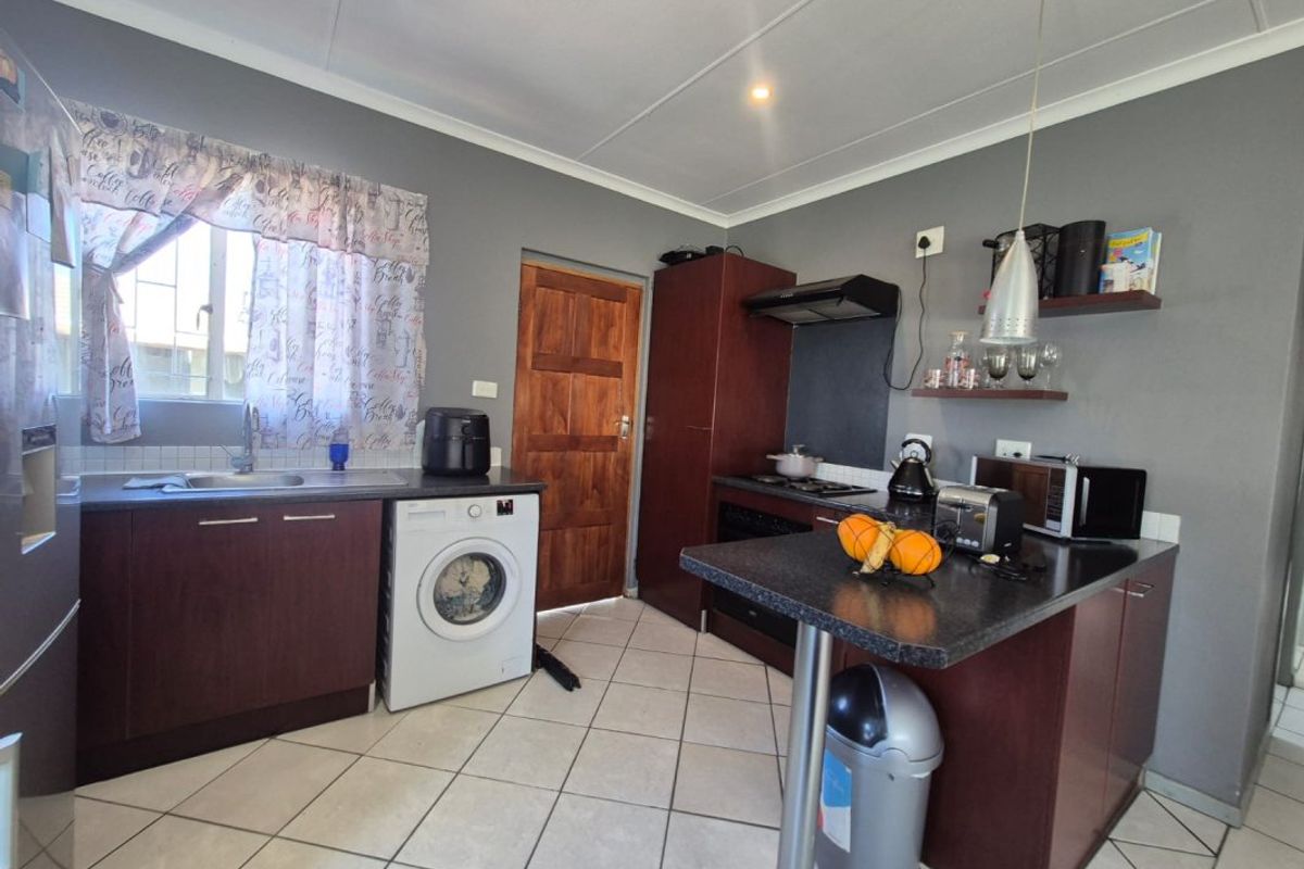 Functional kitchen featuring dark wood cabinetry, a breakfast bar, integrated hob and oven, and tiled flooring.