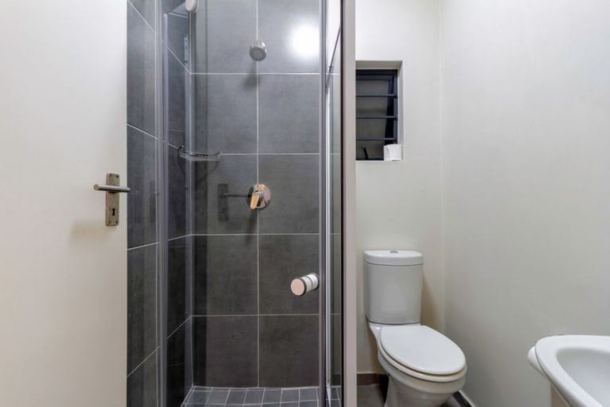 A clean, functional bathroom featuring a glass-enclosed shower with grey tiling, a standard toilet, and a basin.
