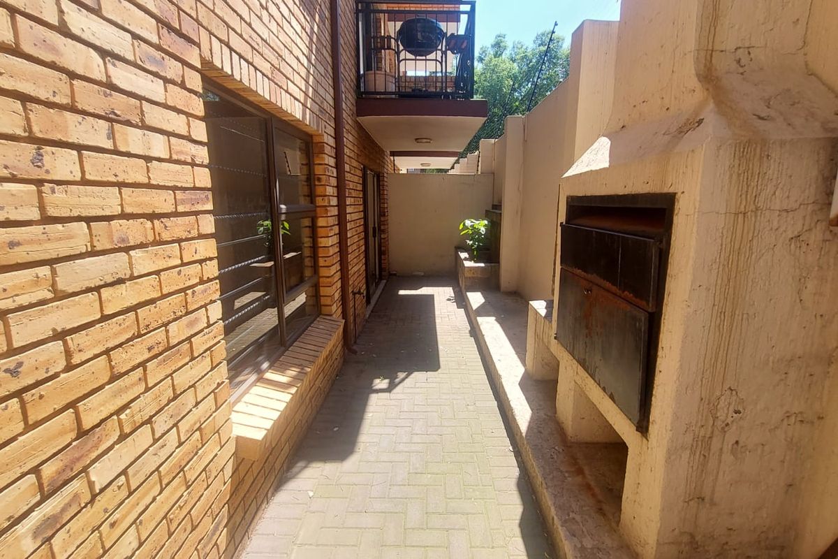 Rear exterior area featuring brick paving, a built-in braai, and access to the townhouse, providing a functional outdoor space for entertaining.