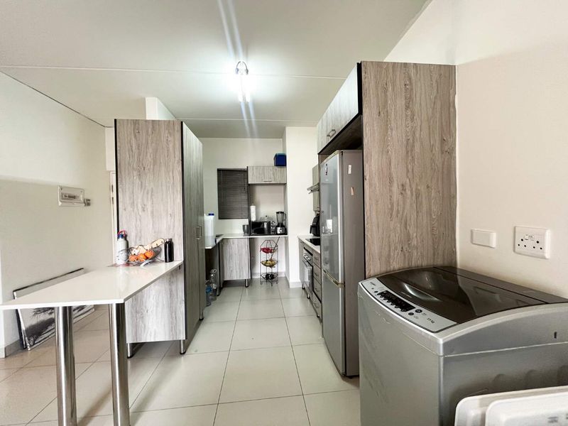 A functional kitchen featuring modern wood-look cabinetry, tiled flooring, a breakfast bar, and integrated appliances, offering a clean and practical workspace.