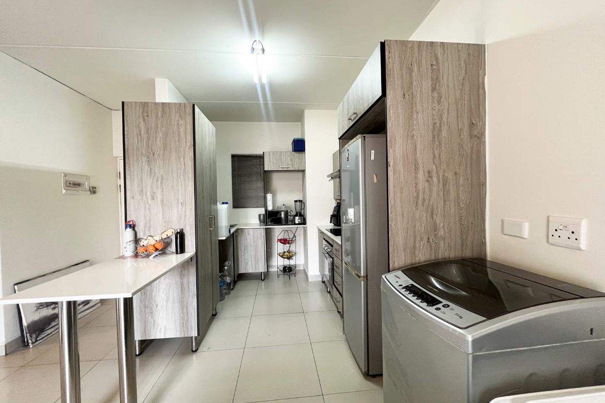 A functional kitchen featuring modern wood-look cabinetry, tiled flooring, a breakfast bar, and integrated appliances, offering a clean and practical workspace.