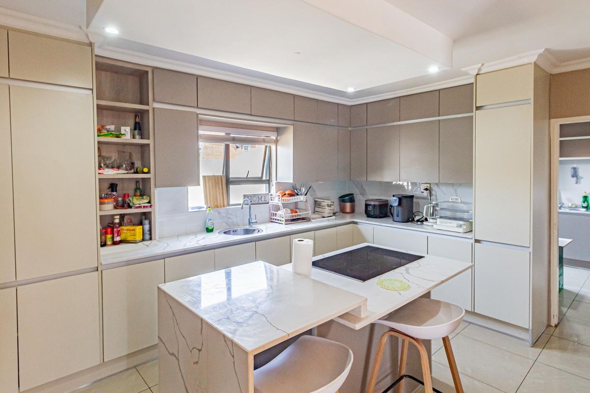 Modern kitchen featuring sleek cabinetry, stone countertops, a central island with an integrated cooktop, and an adjacent scullery area.