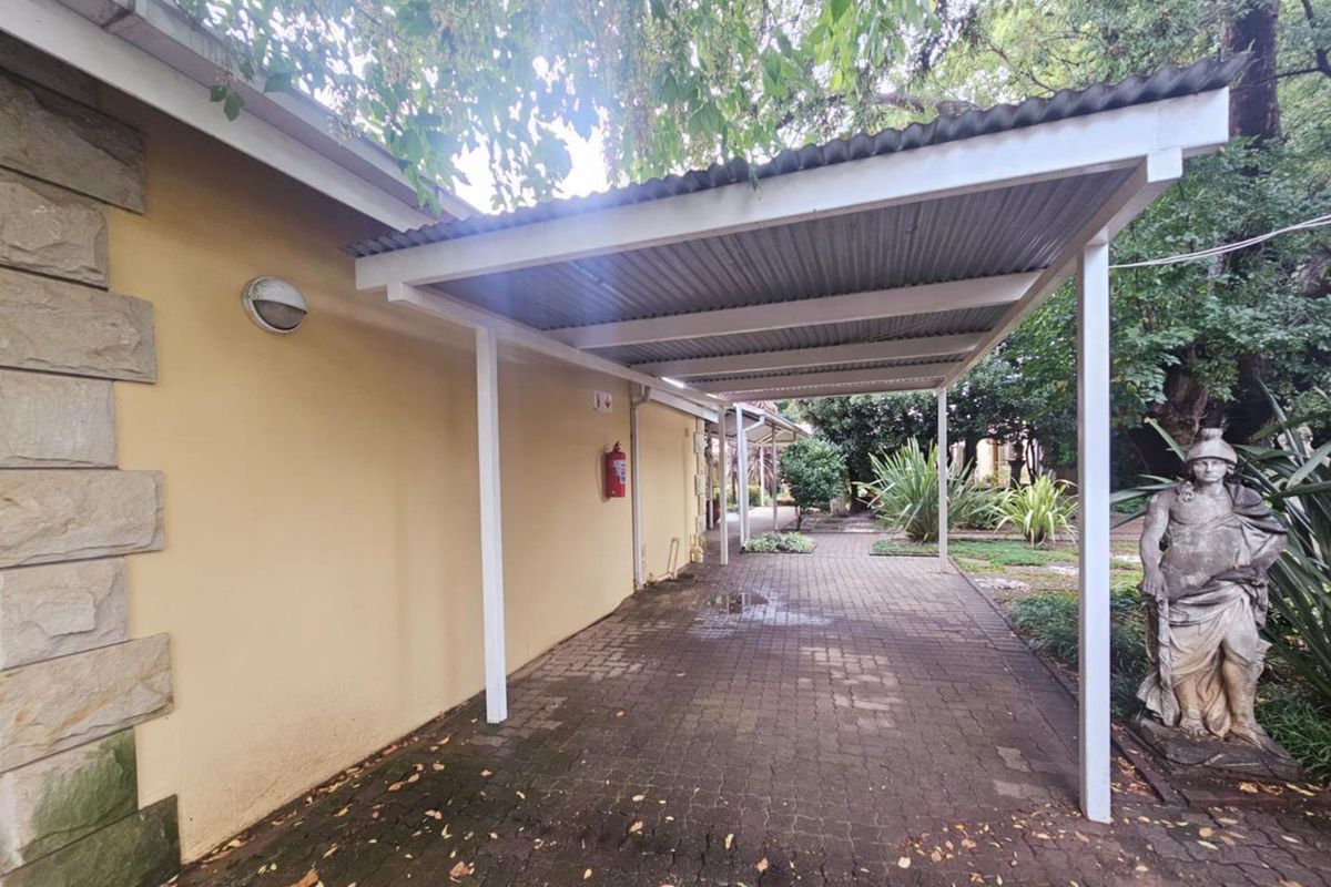 Covered outdoor walkway featuring a corrugated metal roof structure, paved flooring, and exterior wall-mounted lighting.