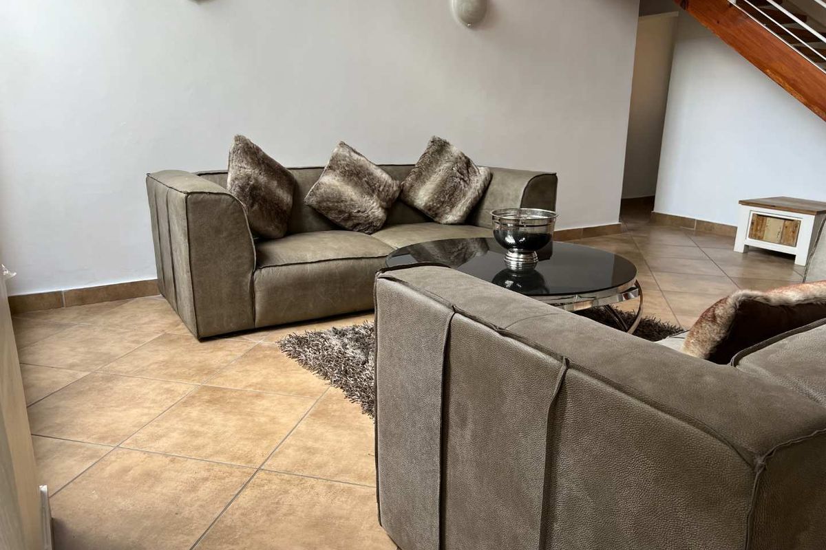 A living room area featuring ceramic floor tiles and a wooden staircase leading to the upper level.