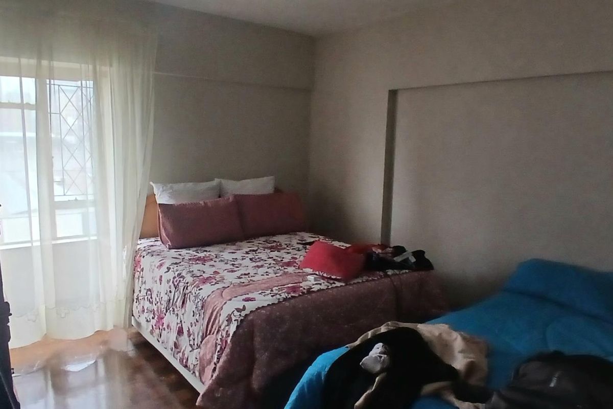 A bedroom featuring laminate flooring and a window with security bars, providing natural light.