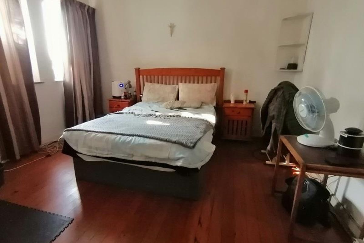 A bedroom featuring polished timber flooring and a built-in wall niche, providing a functional space with natural light.