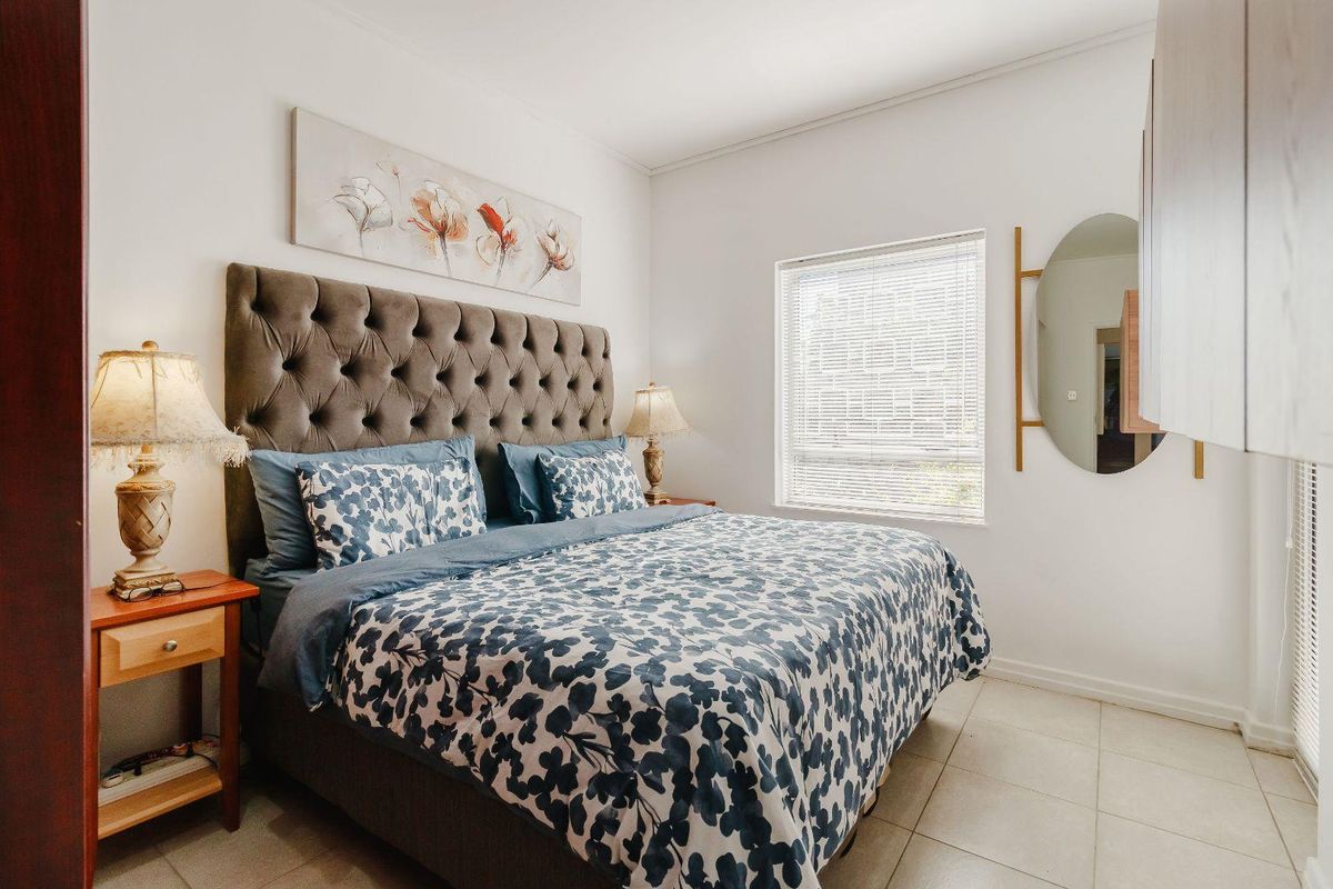A well-lit bedroom featuring tiled flooring, neutral walls, venetian blinds, and built-in cabinetry, offering a clean and functional living space.