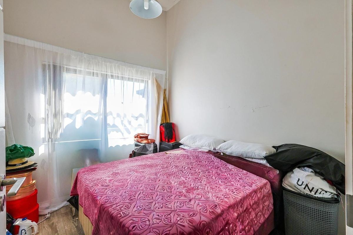 A standard bedroom featuring neutral walls, wood-look flooring, and a large window allowing natural light into the space.