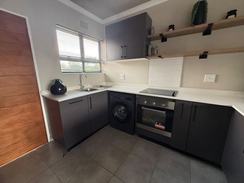 Modern kitchen featuring dark cabinetry, stone countertops, integrated oven and hob, floating shelves, and tiled flooring in a clean, contemporary layout.