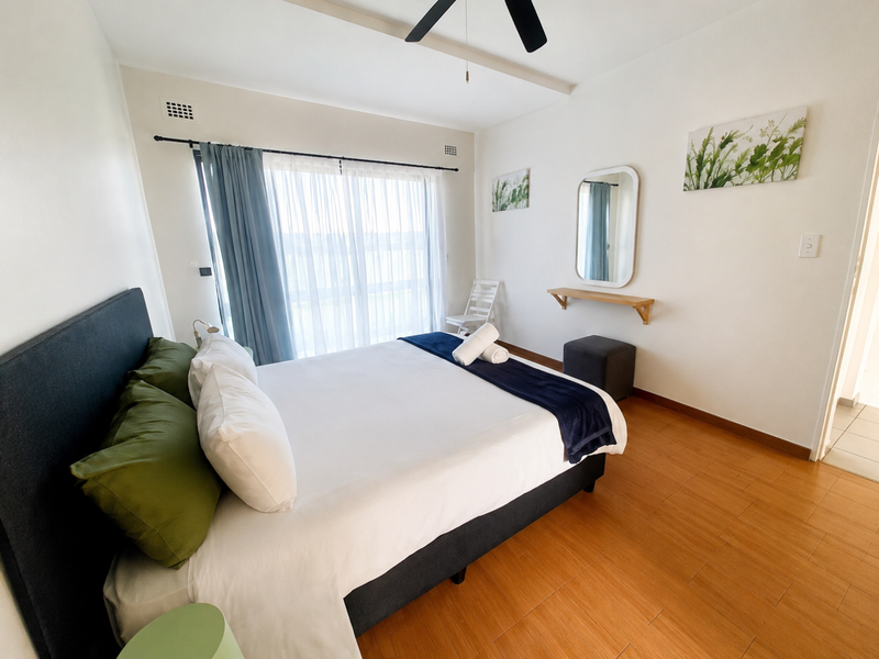 A bright bedroom featuring laminate flooring, a ceiling fan, and a sliding glass door providing natural light.