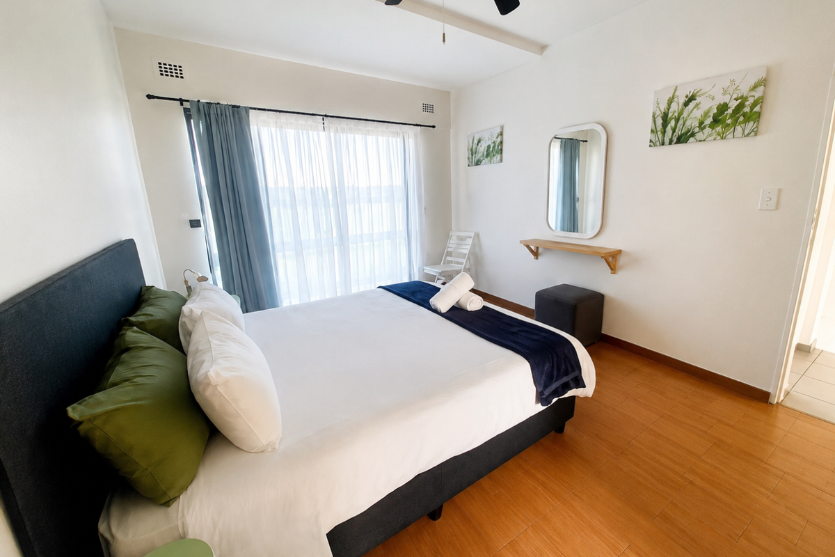 A bright bedroom featuring laminate flooring, a ceiling fan, and a sliding glass door providing natural light.
