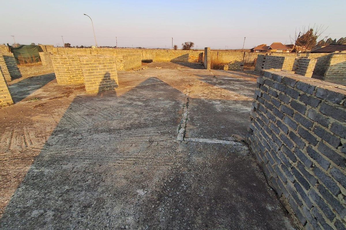 A vacant residential plot featuring an unfinished concrete slab foundation and partial brick perimeter walls, ready for further development.