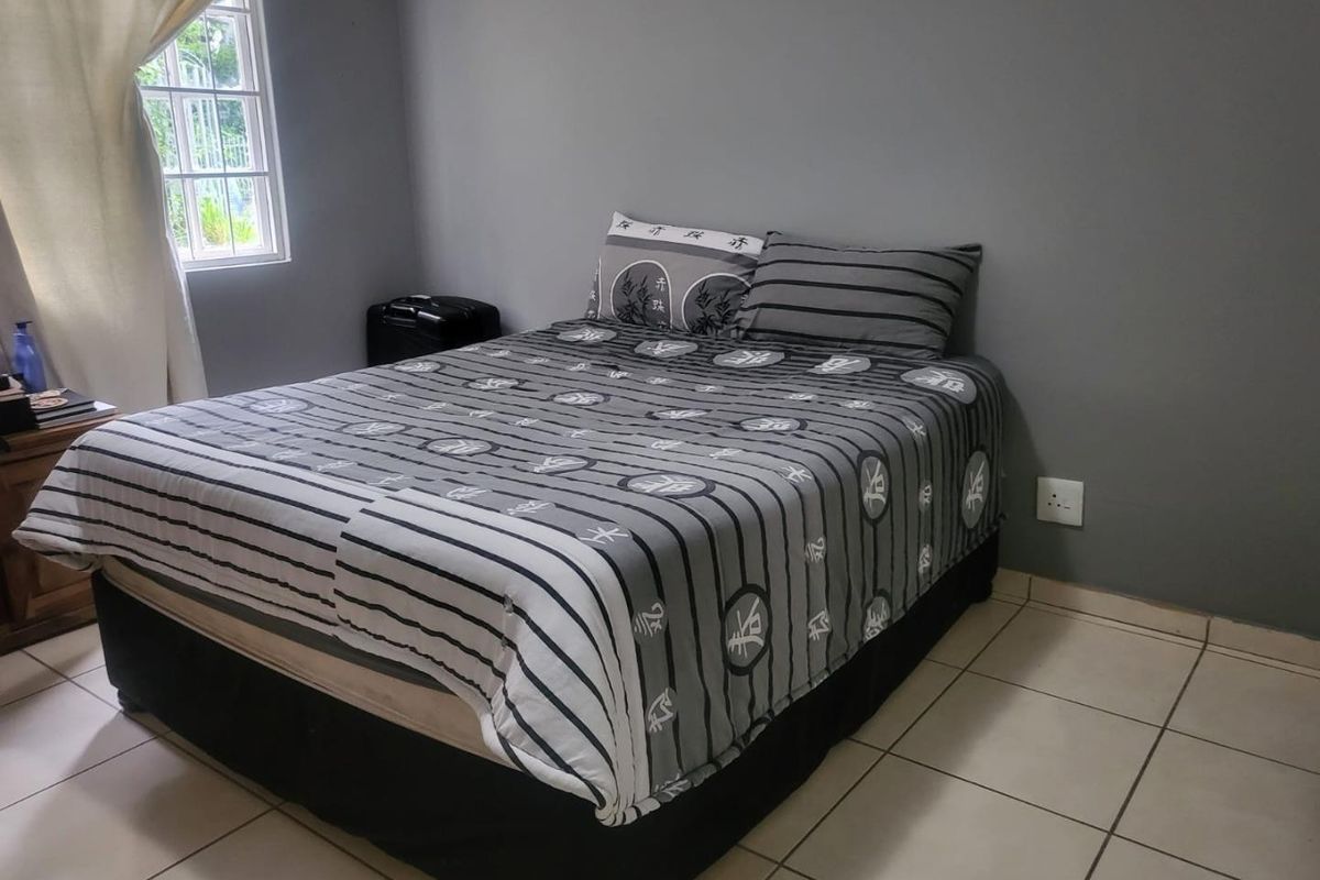 A functional bedroom featuring neutral grey walls, tiled flooring, and a window with security bars, providing a simple and practical living space.