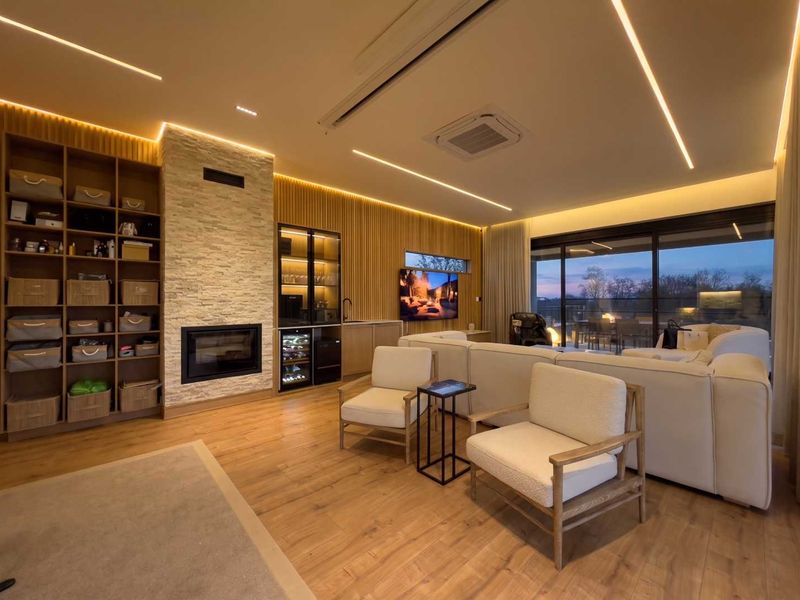 Modern living room featuring a stone-clad fireplace, custom built-in shelving, integrated bar area, recessed LED lighting, and large sliding doors opening to a patio.