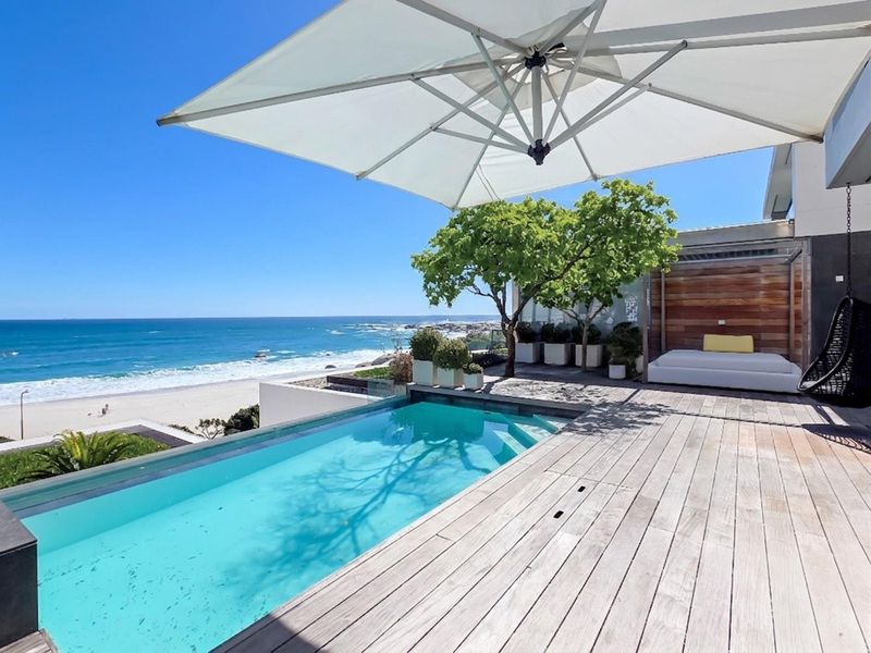 Stunning oceanfront pool area featuring a sleek infinity pool, expansive timber decking, and a glass balustrade overlooking the beach.